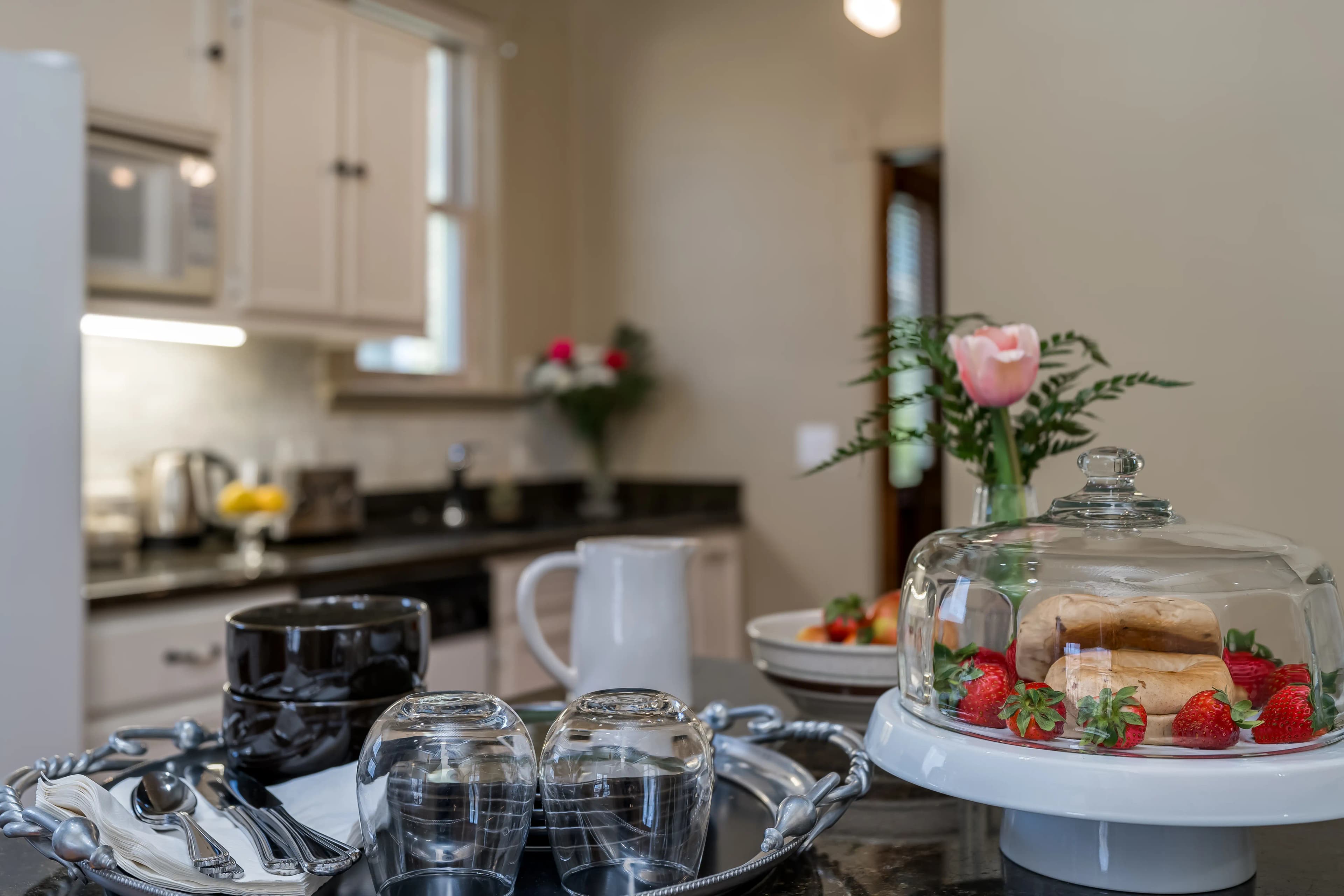 A kitchen counter set up with plates of breakfast breads and fruits, along with glasses, coffee cups, and silverware