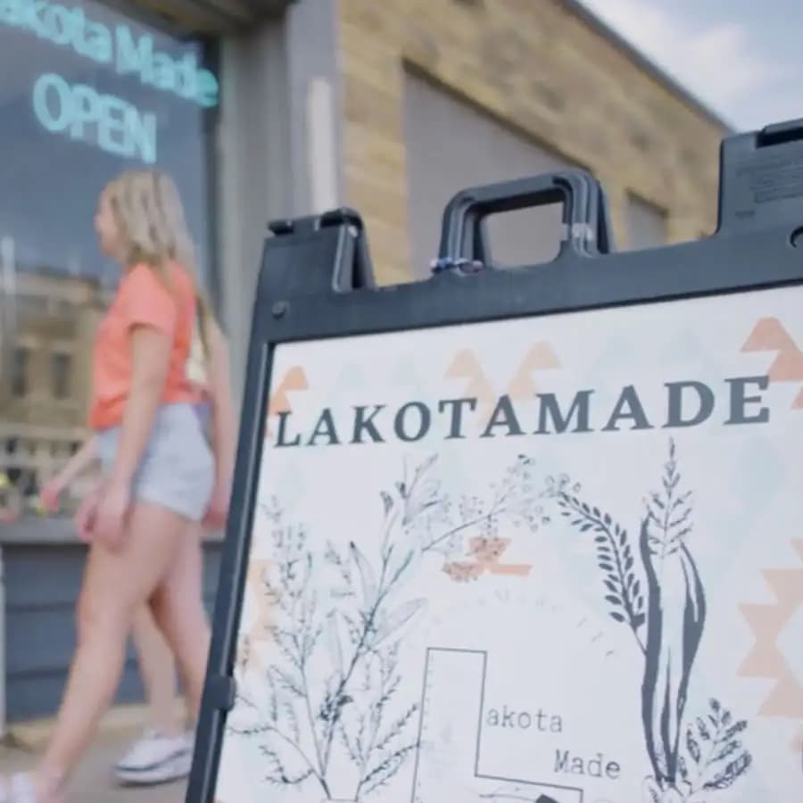 Free standing sign on sidewalk that reads: Lakotamade with two blond girls entering store front.