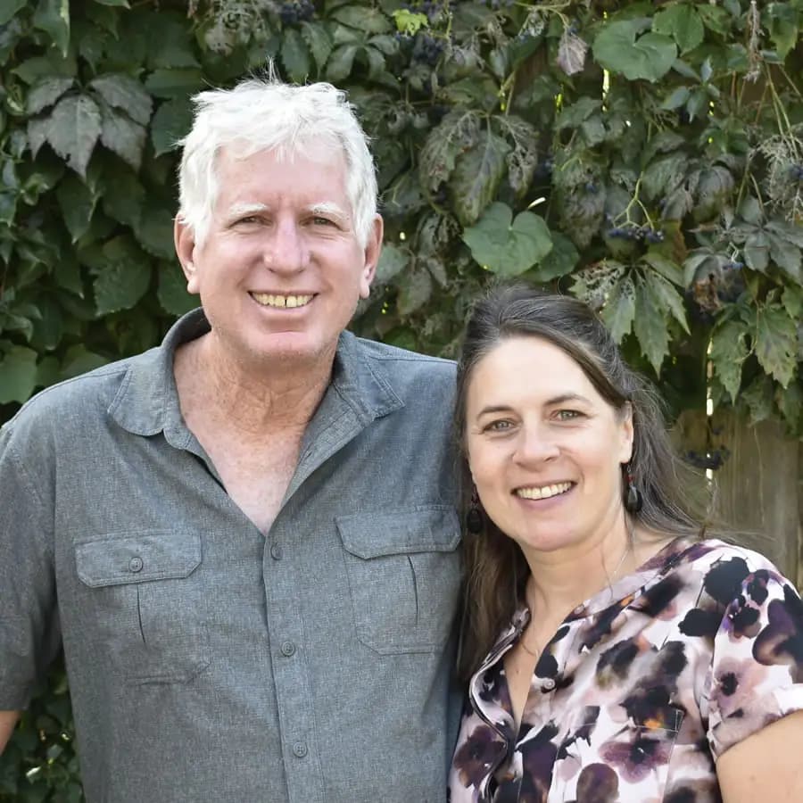 Innkeepers Kristen in floral shirt and chris in grey button down shirt in front of greenery back dr