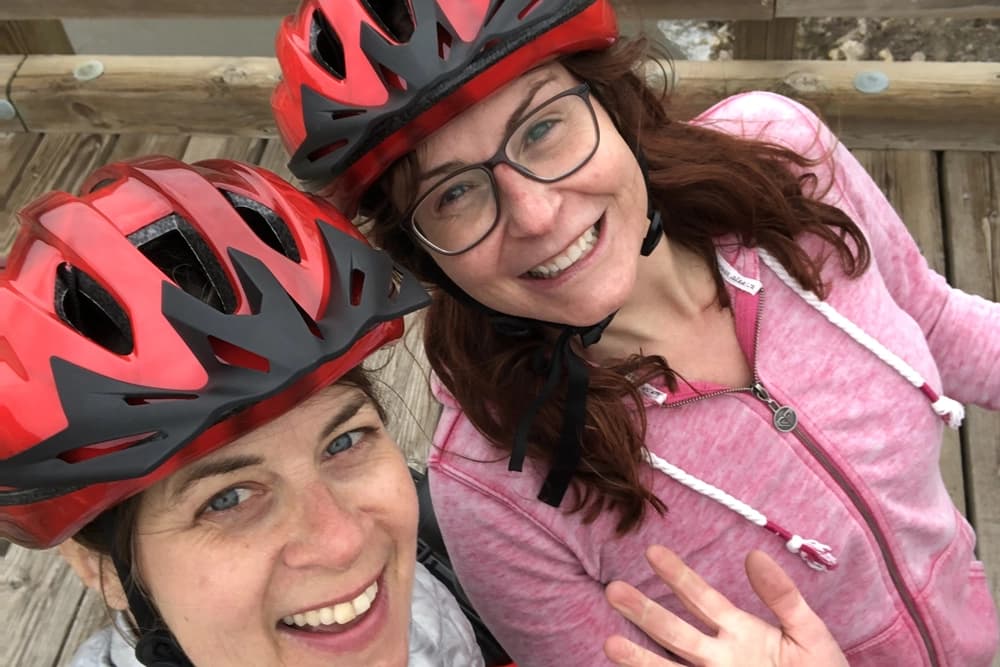 Two women looking up at camera with bike helmets on. 