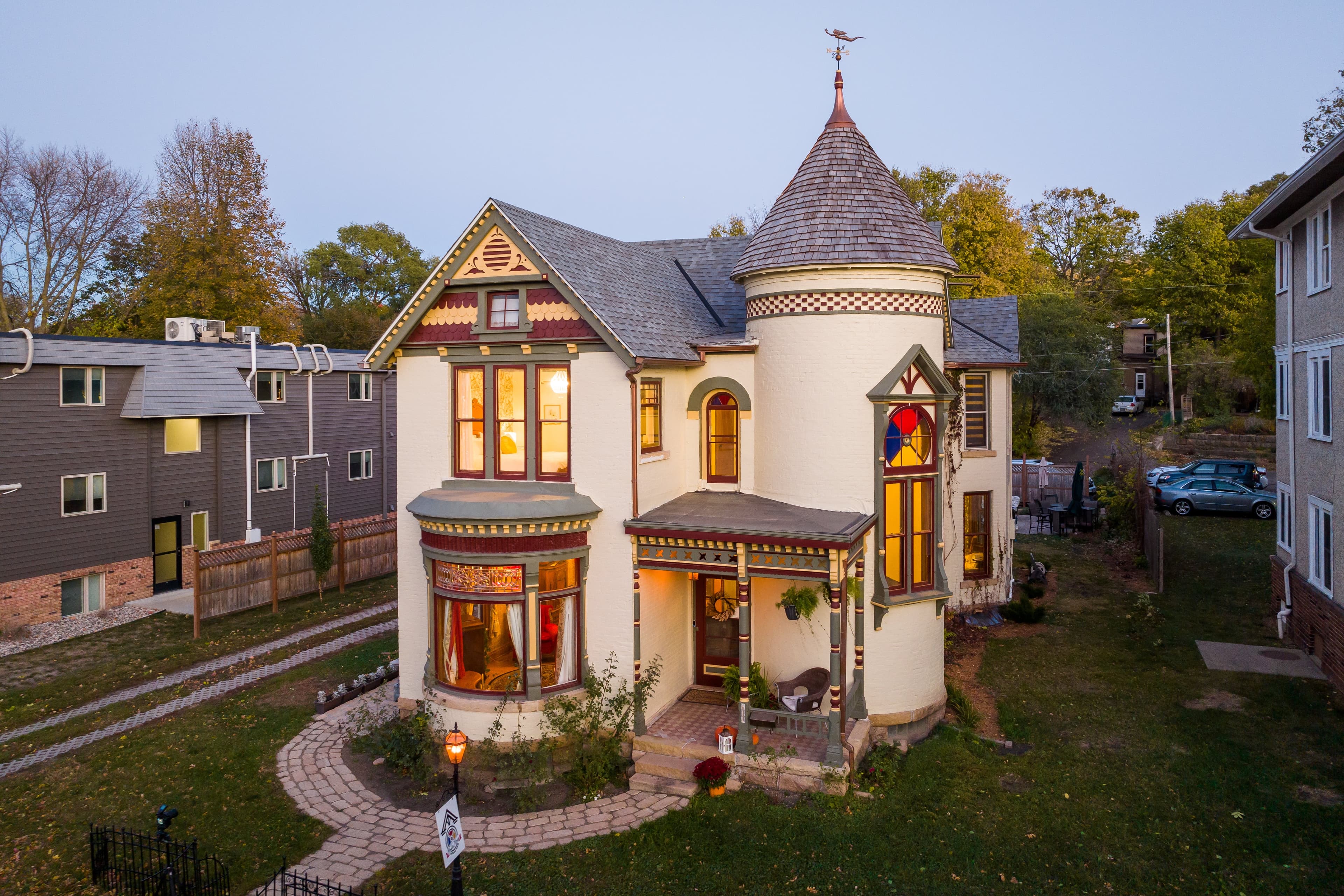 A charming Victorian-style house with a turret and colorful stained glass windows, surrounded by well-kept landscaping.