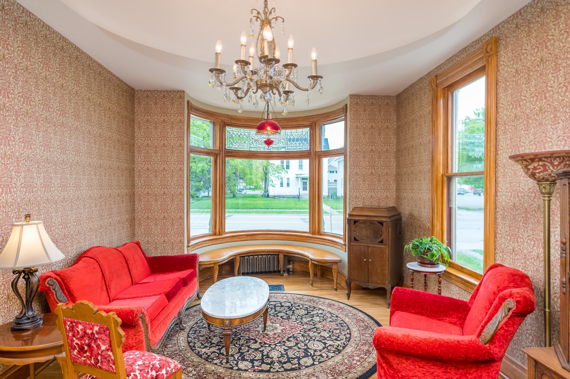 A cozy living room with red furniture, a circular table, and large windows letting in natural light.