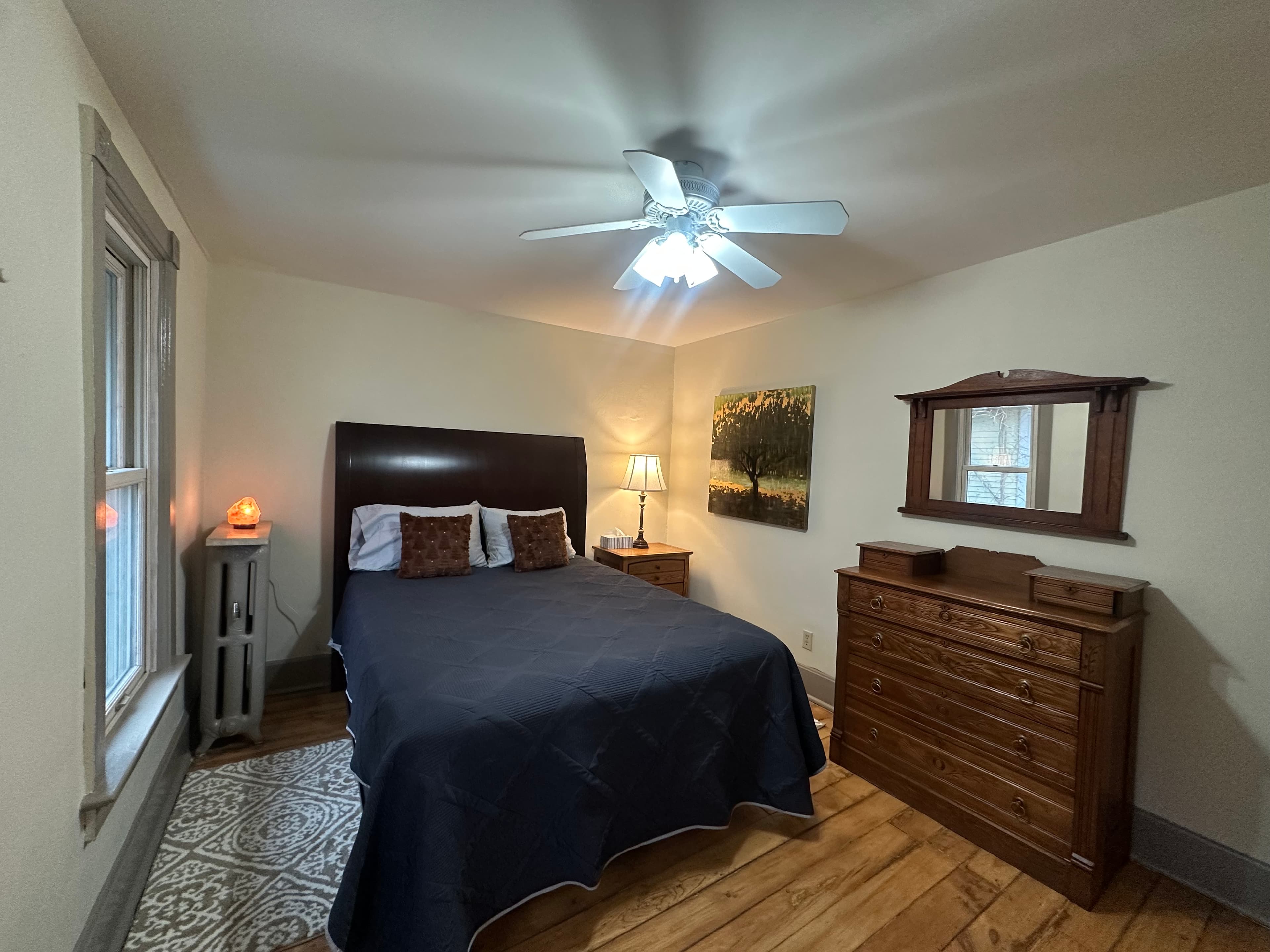 Cozy bedroom featuring a double bed, dresser, lamp, and a decorative painting.