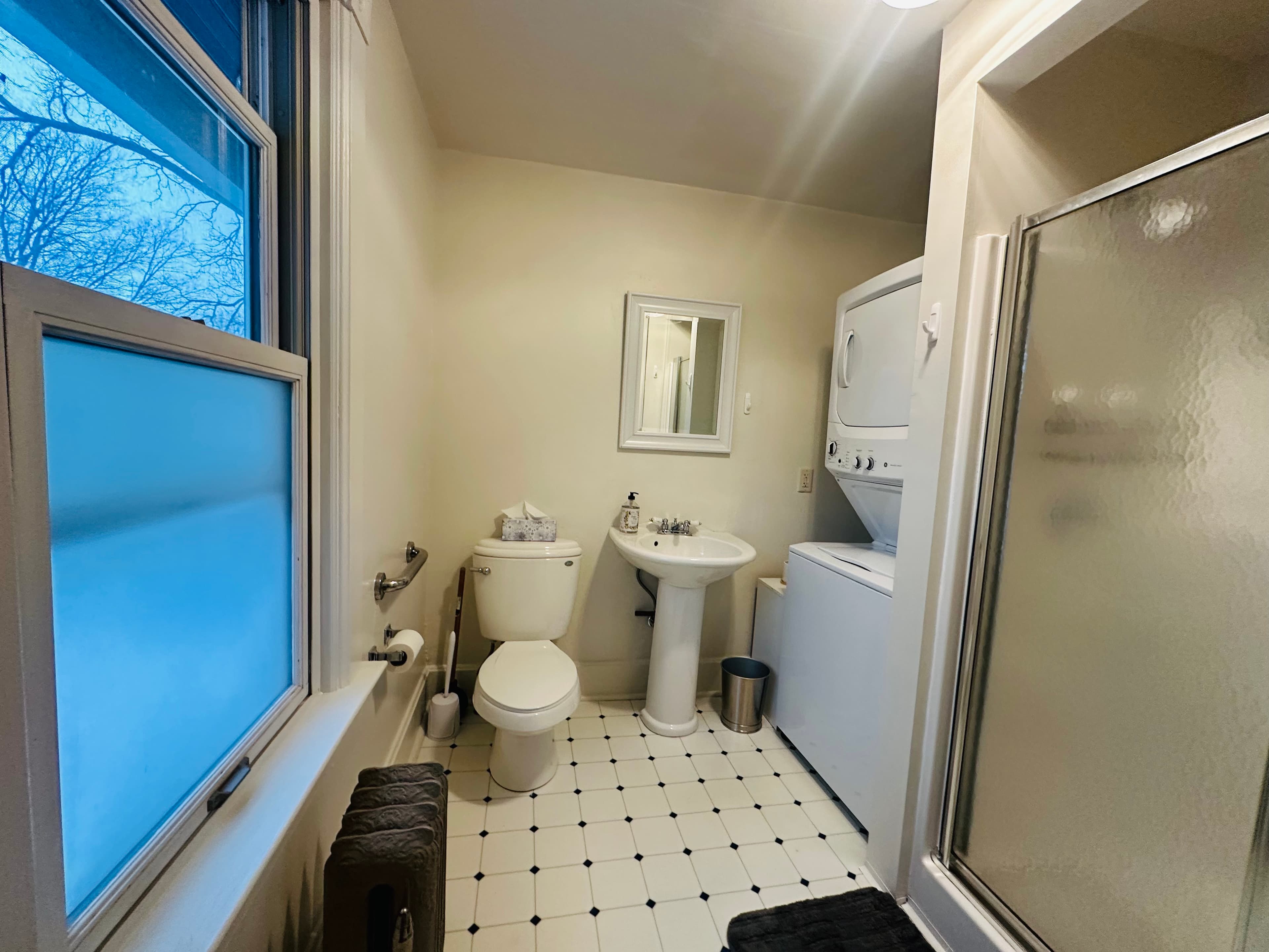 A small bathroom featuring a toilet, sink, shower, and a stacked washer and dryer.