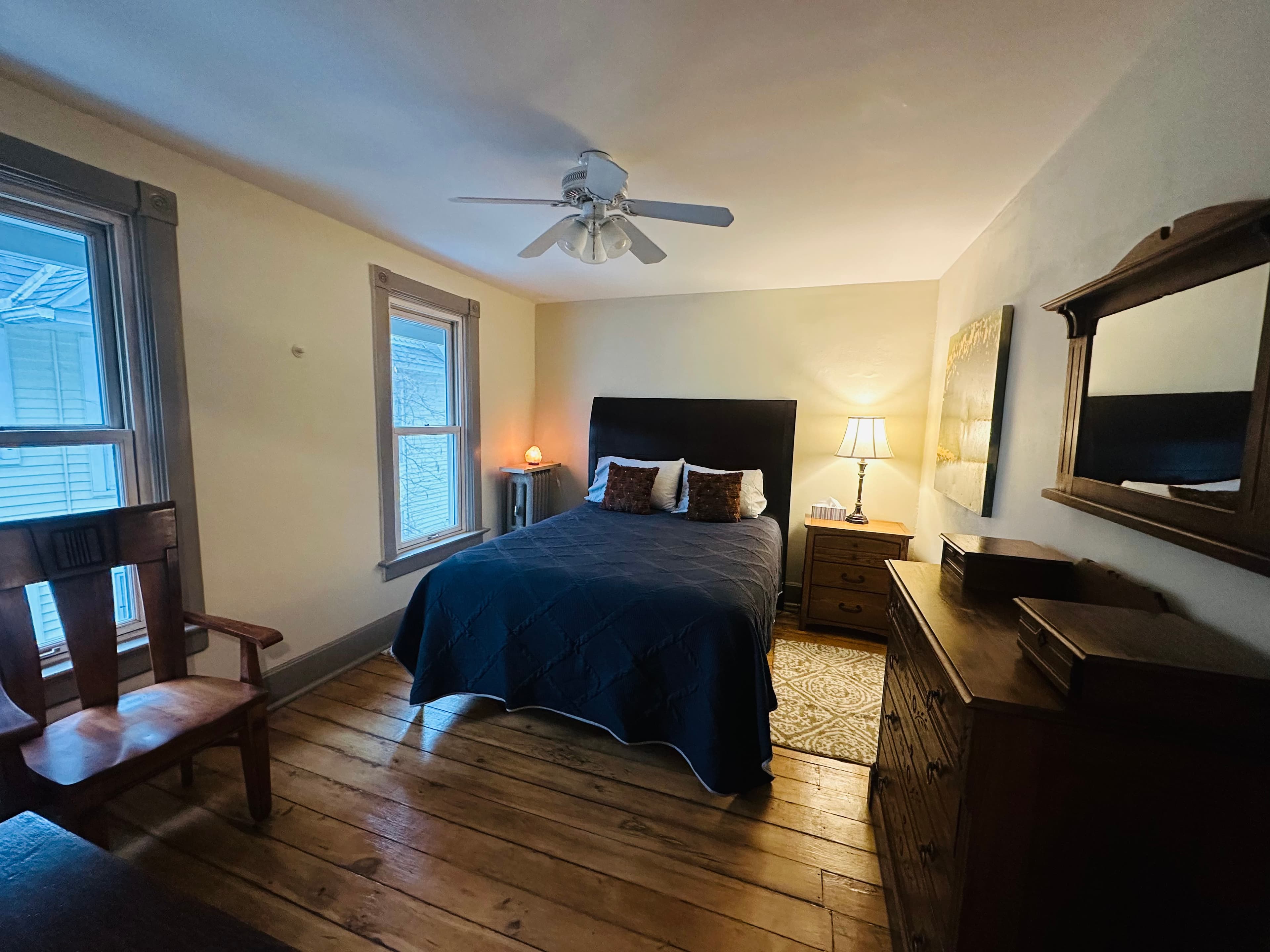 Cozy bedroom featuring a queen bed, wooden furniture, and natural light from windows.