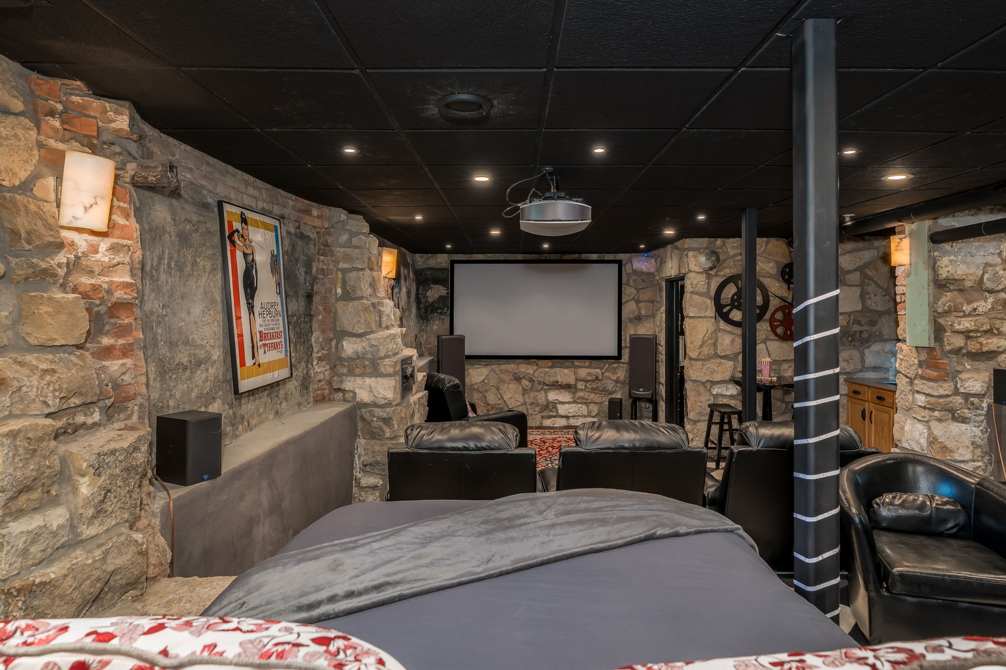 A cozy basement home theater featuring stone walls, a large screen, and comfortable seating.