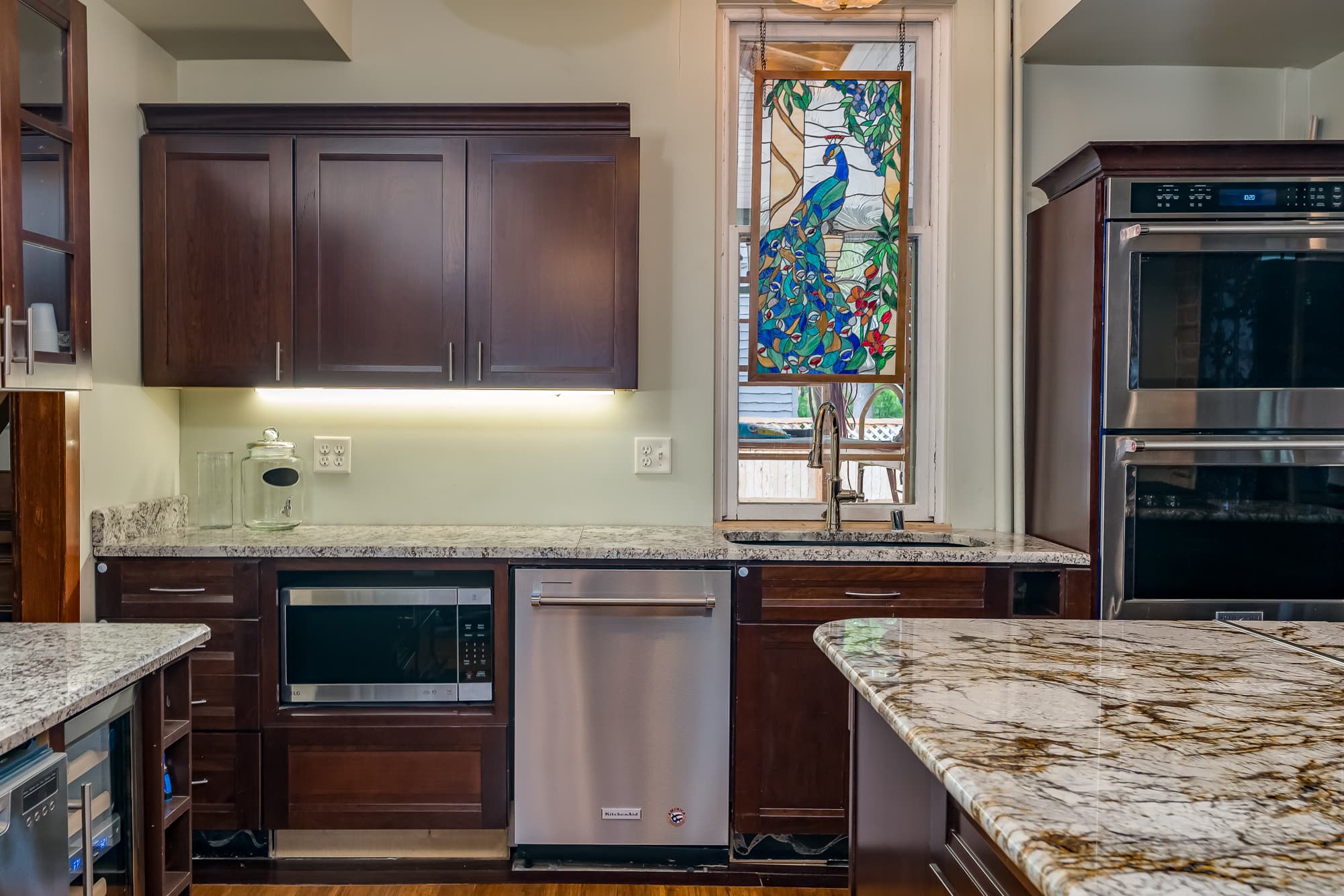 A modern kitchen featuring dark wood cabinets, granite countertops, and a colorful stained glass window.