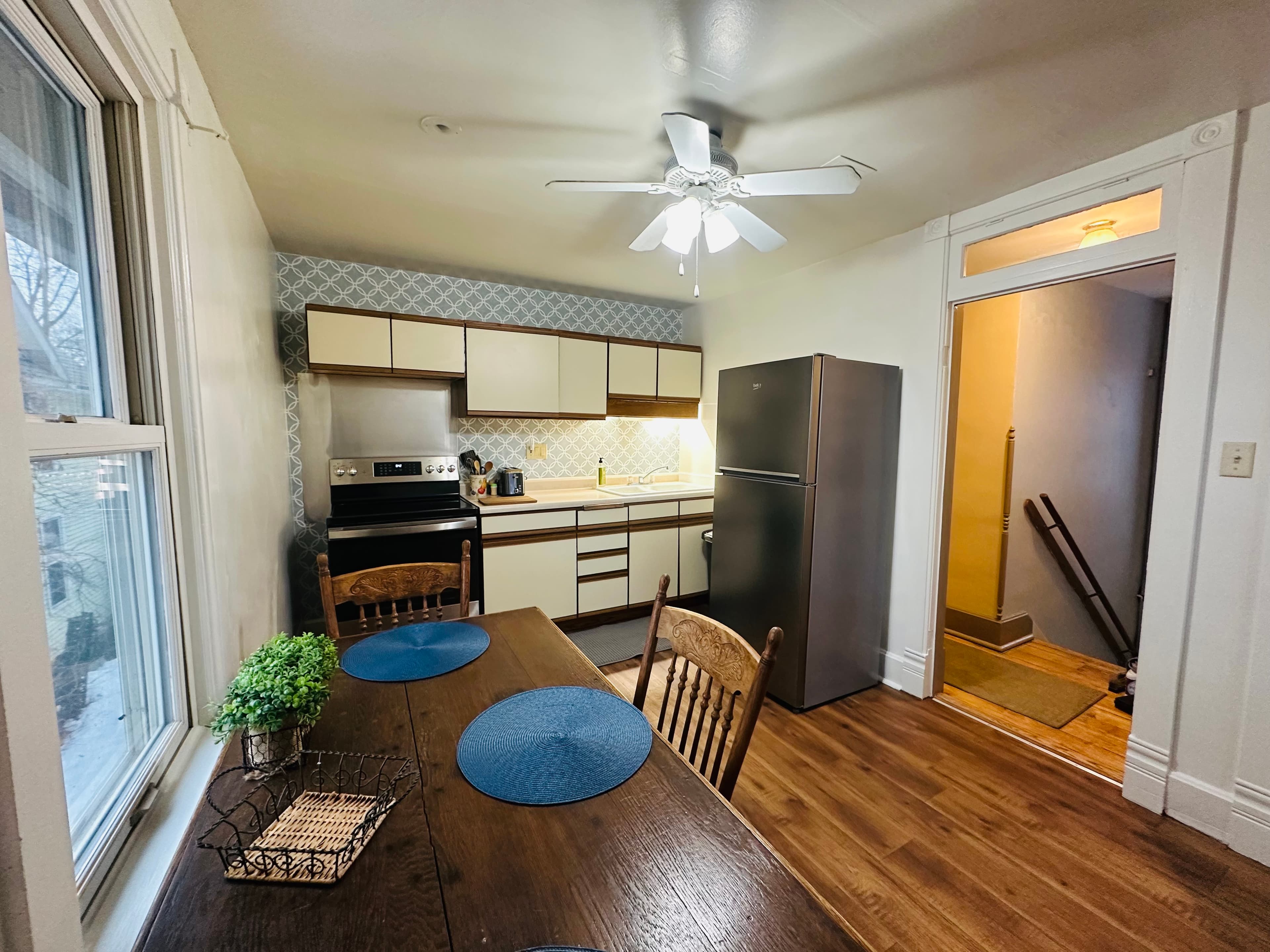 A bright kitchen featuring modern appliances, a dining table, and a door leading to an entrance hallway.