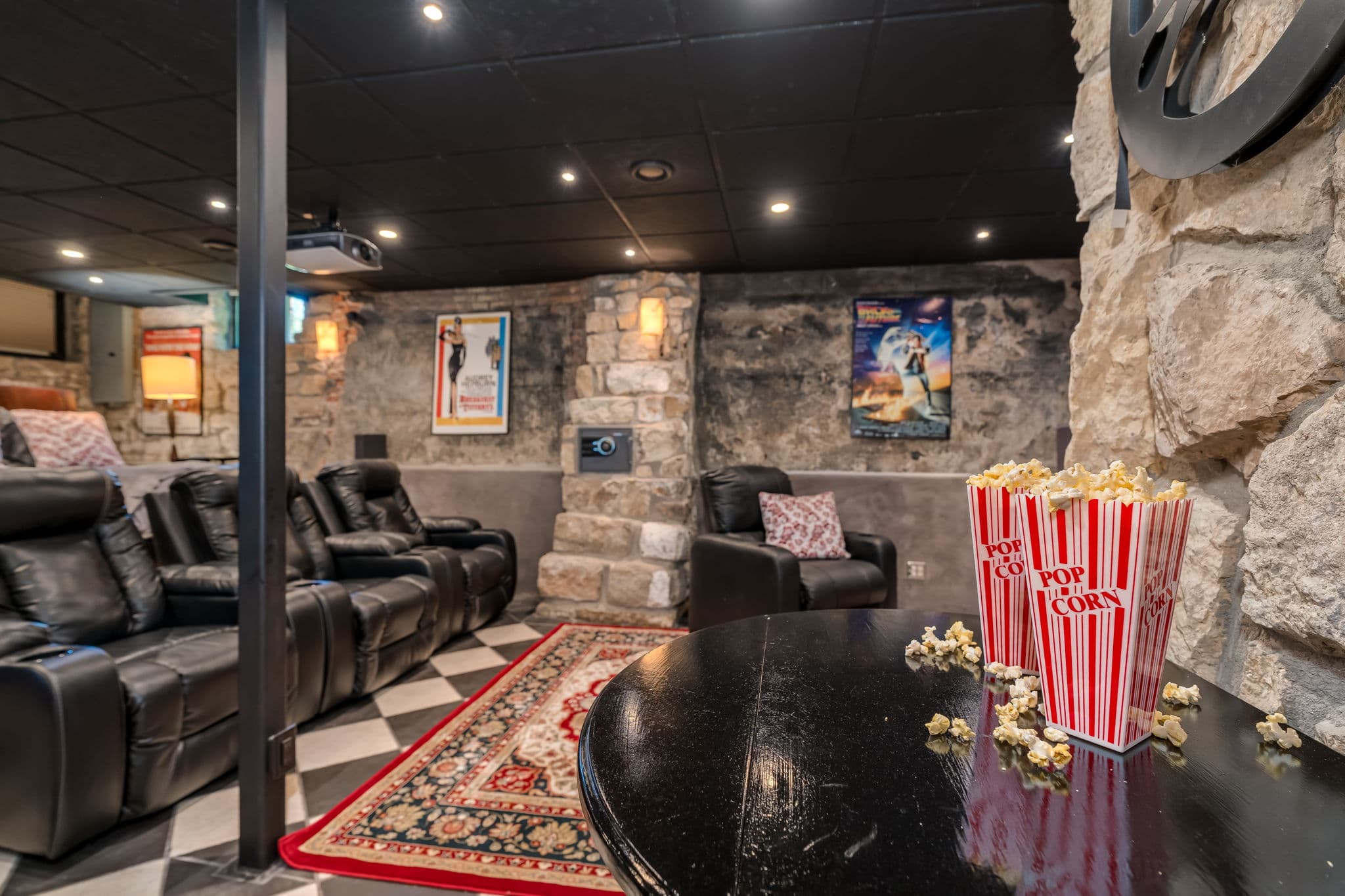 A cozy home theater with leather seating, movie posters, and a table featuring popcorn.