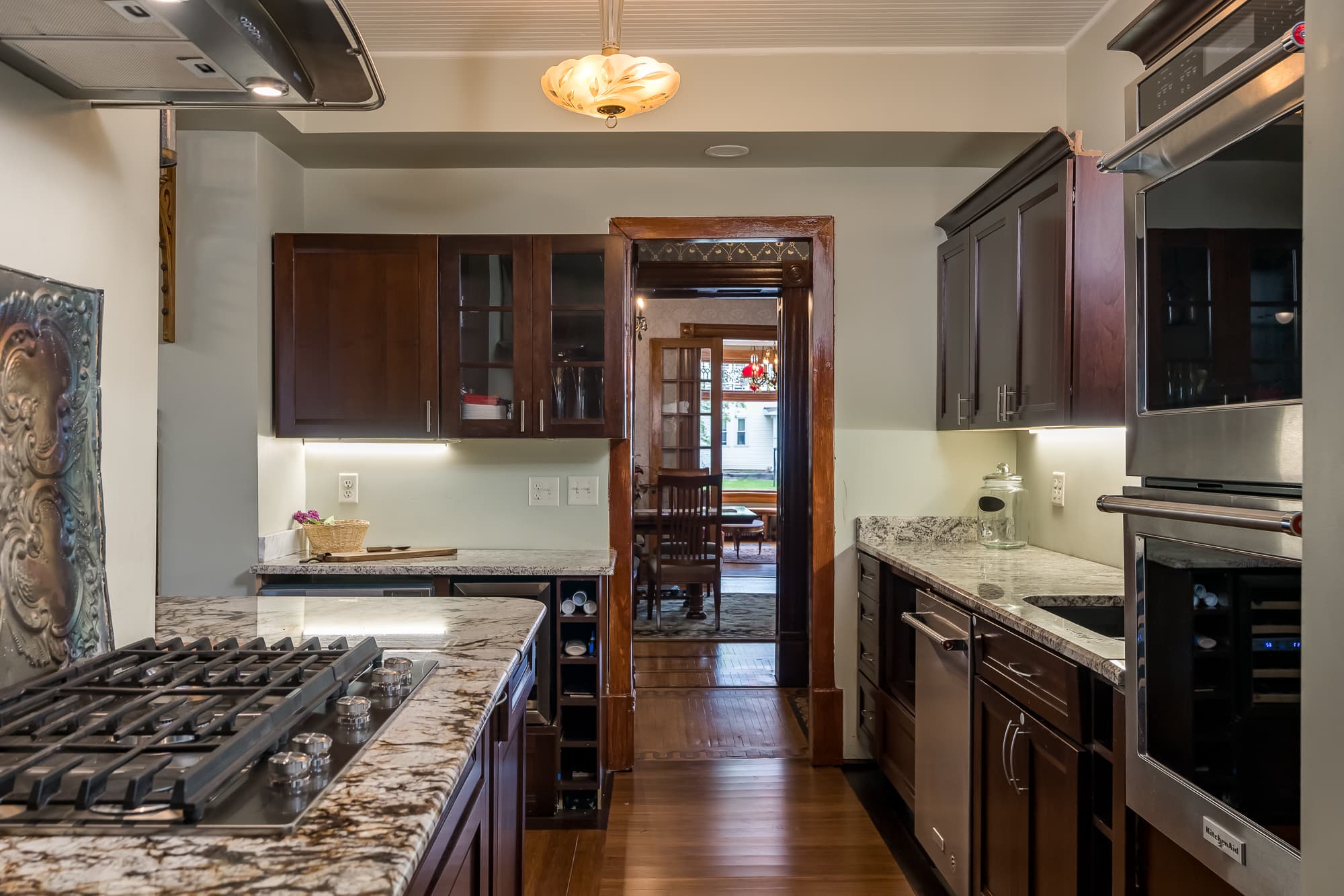 A modern kitchen with dark wood cabinetry, granite countertops, and stainless steel appliances, leading to a dining area.